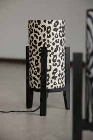 Eruca 34cm Leopard bordlampe Fra Markslöjd - Lampefoden i sort tr&aelig; er kombineret med en cylindrisk tekstilsk&aelig;rm i off-white og brunt leopardm&oslash;nster, hvilket giver lampen en trendy og personlig karakter.