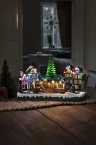 Mekanisk Juledekoration Med Julemarked 24cm Flerfarvet Fra Konstsmide - Med 28 varmhvide LED-lys, overd&aelig;kkede huse, farverige markedsboder og et k&aelig;mpe juletr&aelig; i centrum spreder det b&aring;de lys og musik.
