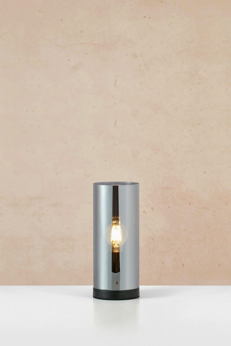 Post 38cm Røgfarvet bordlampe Fra Markslöjd - Post er en stilfuld cylindrisk bordlampe, med fod i matsort metal og skærm af røget glas.