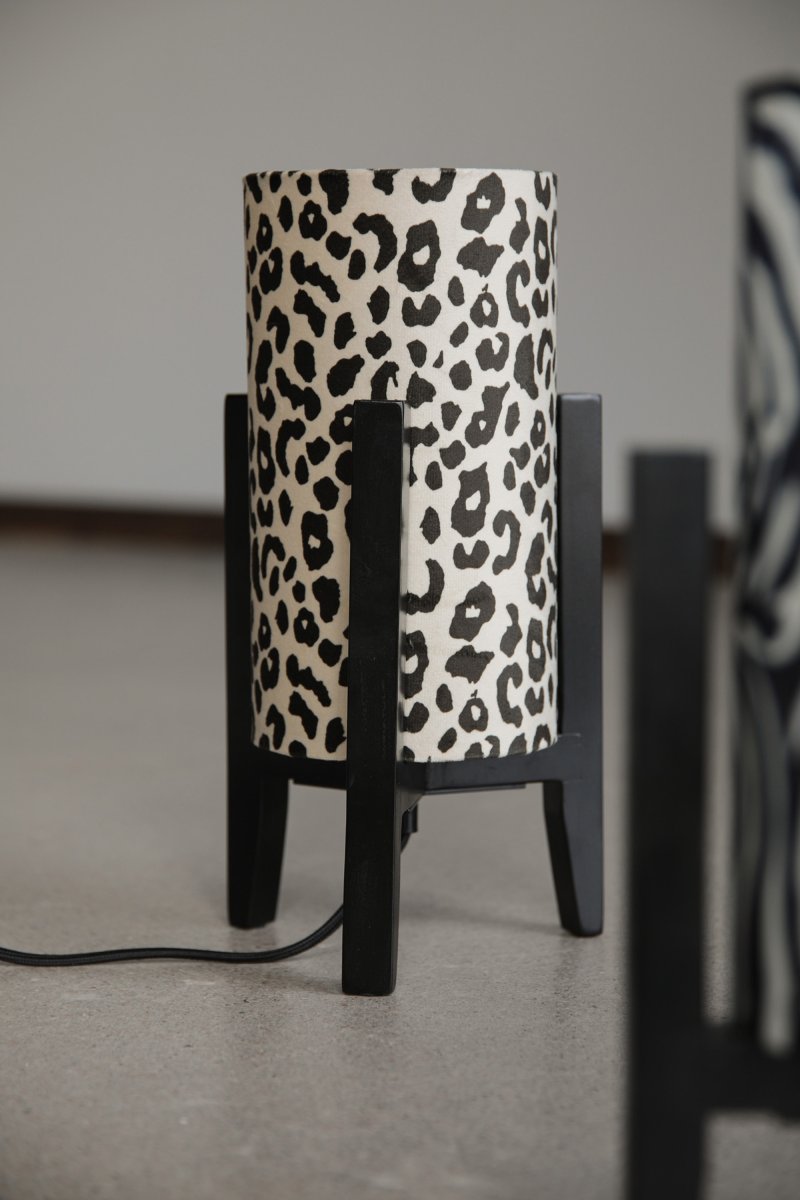 Eruca 34cm Leopard bordlampe Fra Markslöjd - Lampefoden i sort tr&aelig; er kombineret med en cylindrisk tekstilsk&aelig;rm i off-white og brunt leopardm&oslash;nster, hvilket giver lampen en trendy og personlig karakter.
