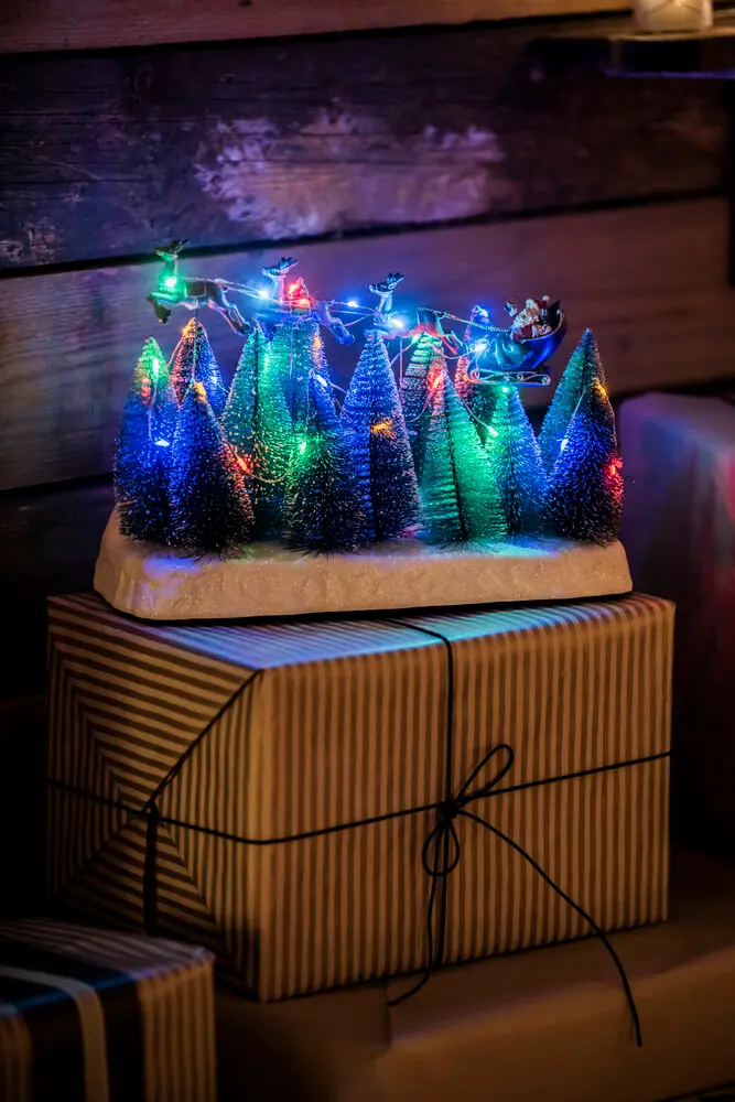 Nisse Med Slæde 22cm Flerfarvet Fra Konstsmide - Juledekoration med julemanden i en flyverdragt, der flyver over snekl&aelig;dte grantr&aelig;er.
