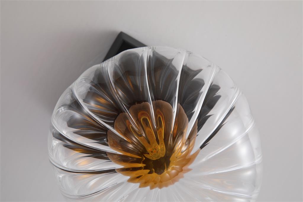 Sunbeam Ø14 Gennemsigtig/sort væglampe Fra Searchlight - Den runde, ribbede skærm i transparent glas har en smuk ravfarvet kuppel indeni, der skaber liv og struktur, samtidig med at den spreder lyset blødt og behageligt i rummet.
