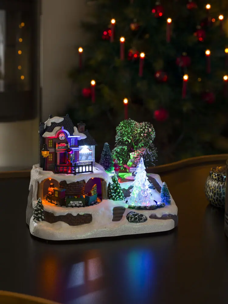 Mekanisk Juledekoration Med Togstation 17cm Flerfarvet Fra Konstsmide - Tr&aelig;d ind i en vinterlig miniatureverden med denne mekaniske juledekoration &ndash; en charmerende togstation i rolige omgivelser.