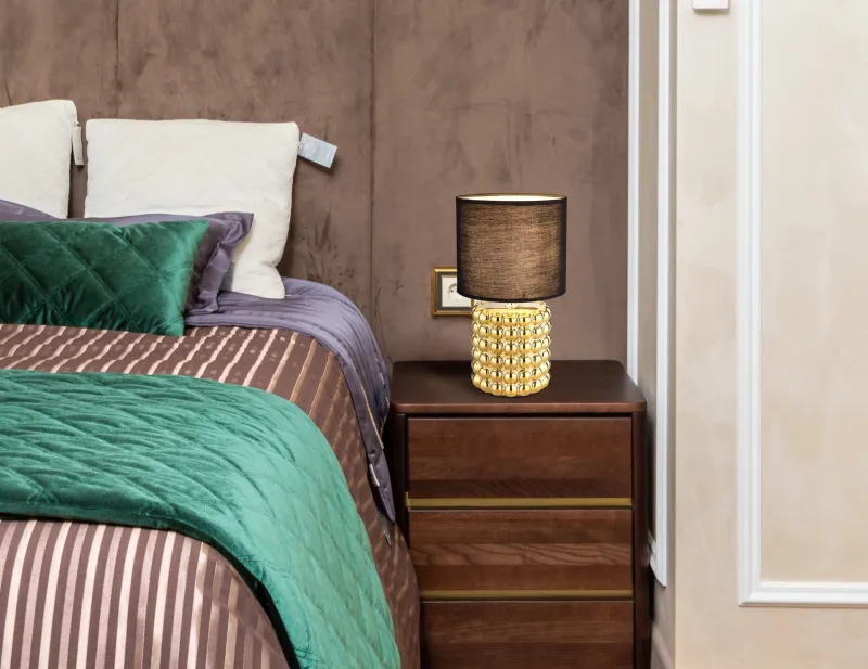 Valentino 33cm Guld bordlampe Fra Globo Lighting - P&aring; en cylinderformad fot i guldf&auml;rgad keramik vilar en stilren, svart textilsk&auml;rm.