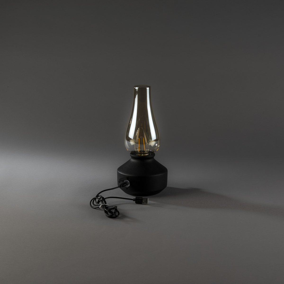 Genopladelig bordlampe 25cm Sort bærbar Fra Konstsmide - Lampen er lavet af metal og glas med en sort lampebase og en praktisk lysdæmper, der gør det nemt at justere det varme hvide, atmosfæriske lys.