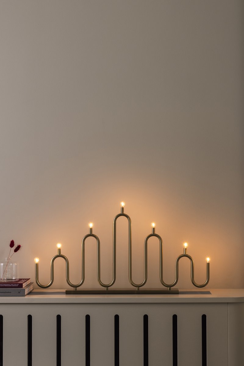 Noel 7 Messing Fra Globen Lighting - Det bløde, bølgede design er skabt af metalrør, der er bøjet i hånden på forskellige niveauer, og giver en moderne fortolkning af den klassiske adventslysholder.