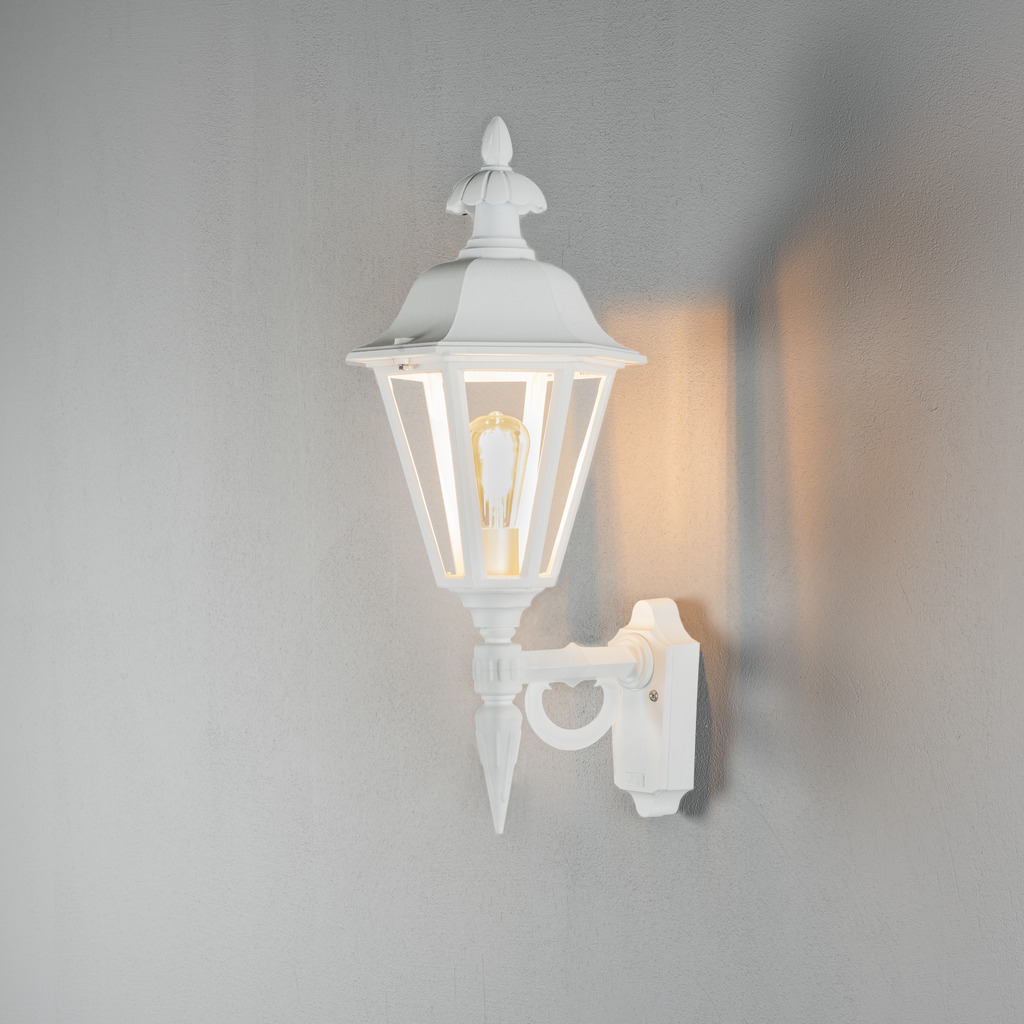 Pallas Hvid udendørslampe Fra Konstsmide - Med sit lanterneformede design og klare glaspaneler spreder lampen et varmt og indbydende lys, der er perfekt til indgange, terrasser og gangbroer.