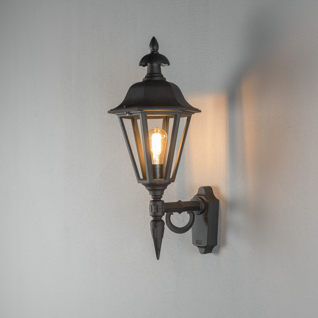 Pallas Sort udendørslampe Fra Konstsmide - Med sit lanterneformede design og klare glaspaneler spreder lampen et varmt og indbydende lys, der er perfekt til indgange, terrasser og gangbroer.