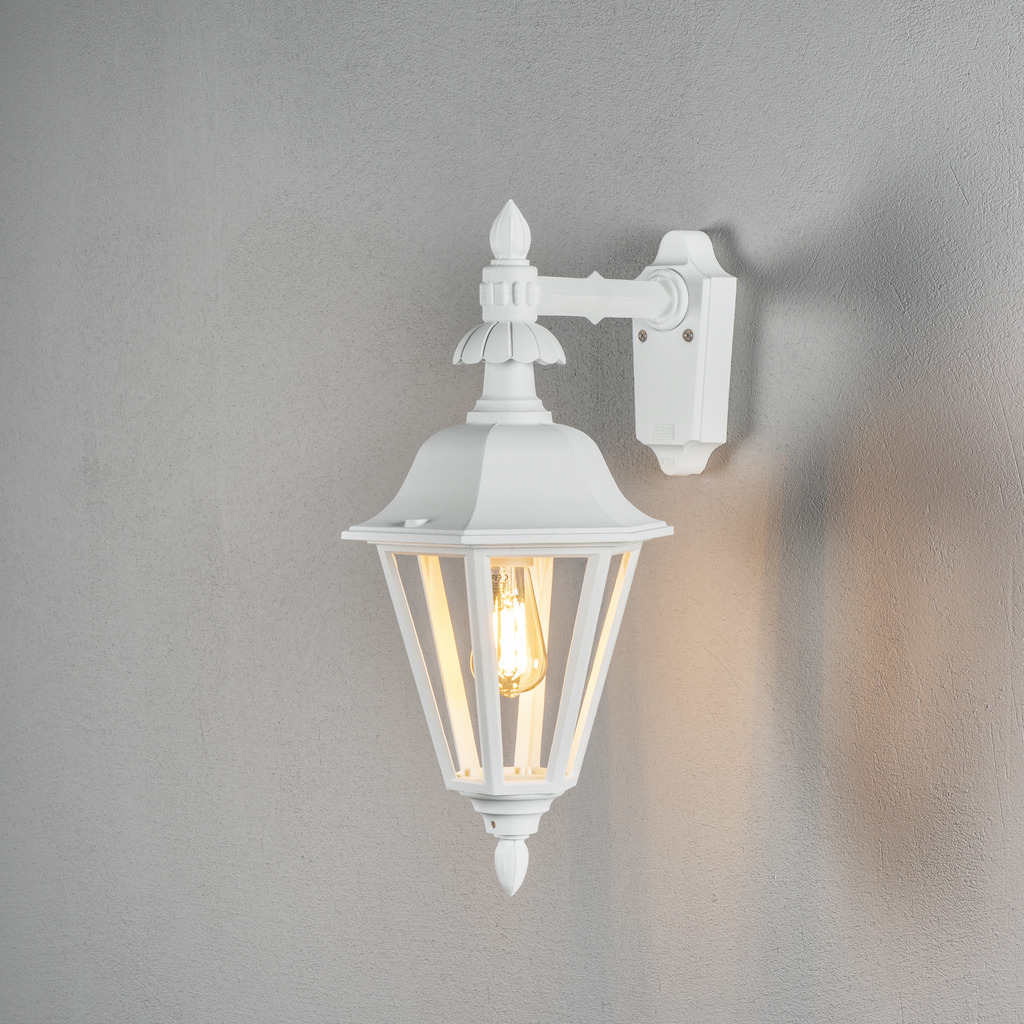 Pallas Hvid udendørslampe Fra Konstsmide - Med sit lanterneformede design og klare glaspaneler spreder lampen et varmt og indbydende lys, der er perfekt til indgange, terrasser og gangbroer.