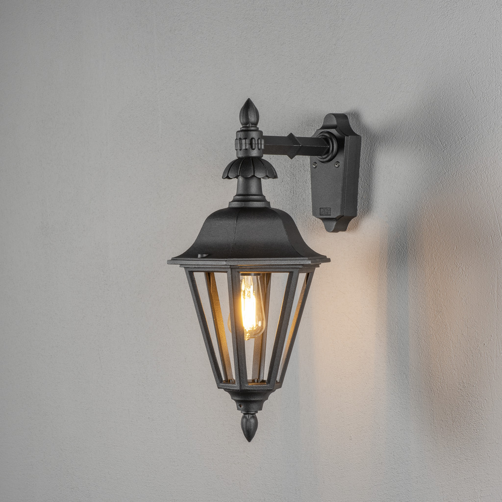 Pallas Sort udendørslampe Fra Konstsmide - Med sit lanterneformede design og klare glaspaneler spreder lampen et varmt og indbydende lys, der er perfekt til indgange, terrasser og gangbroer.
