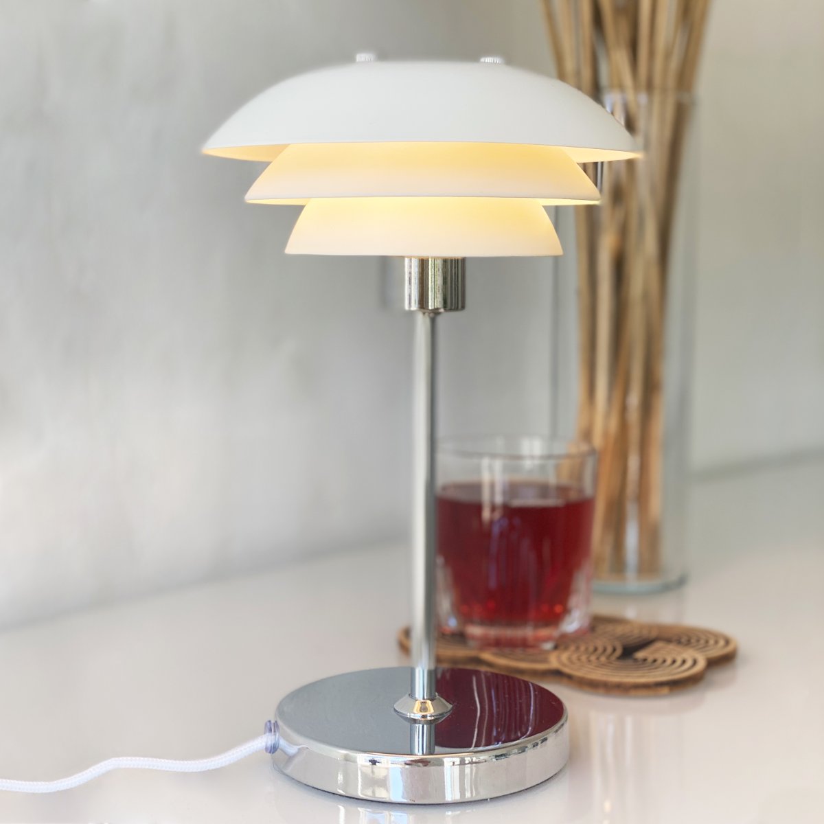 DL16 25cm Hvid bordlampe Fra Dyberg Larsen - Skærmene er lavet af metal og bunden i krom, med farvemulighederne sort og hvid.