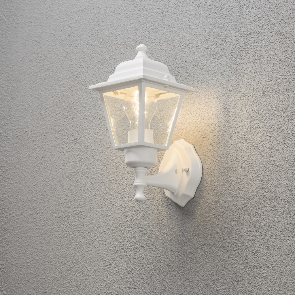Vägglykta Hvid udendørslampe Fra Konstsmide - Med sit lanterneformede design og klare glaspaneler spreder lampen et varmt og indbydende lys, der er perfekt til indgange, terrasser og gangbroer.