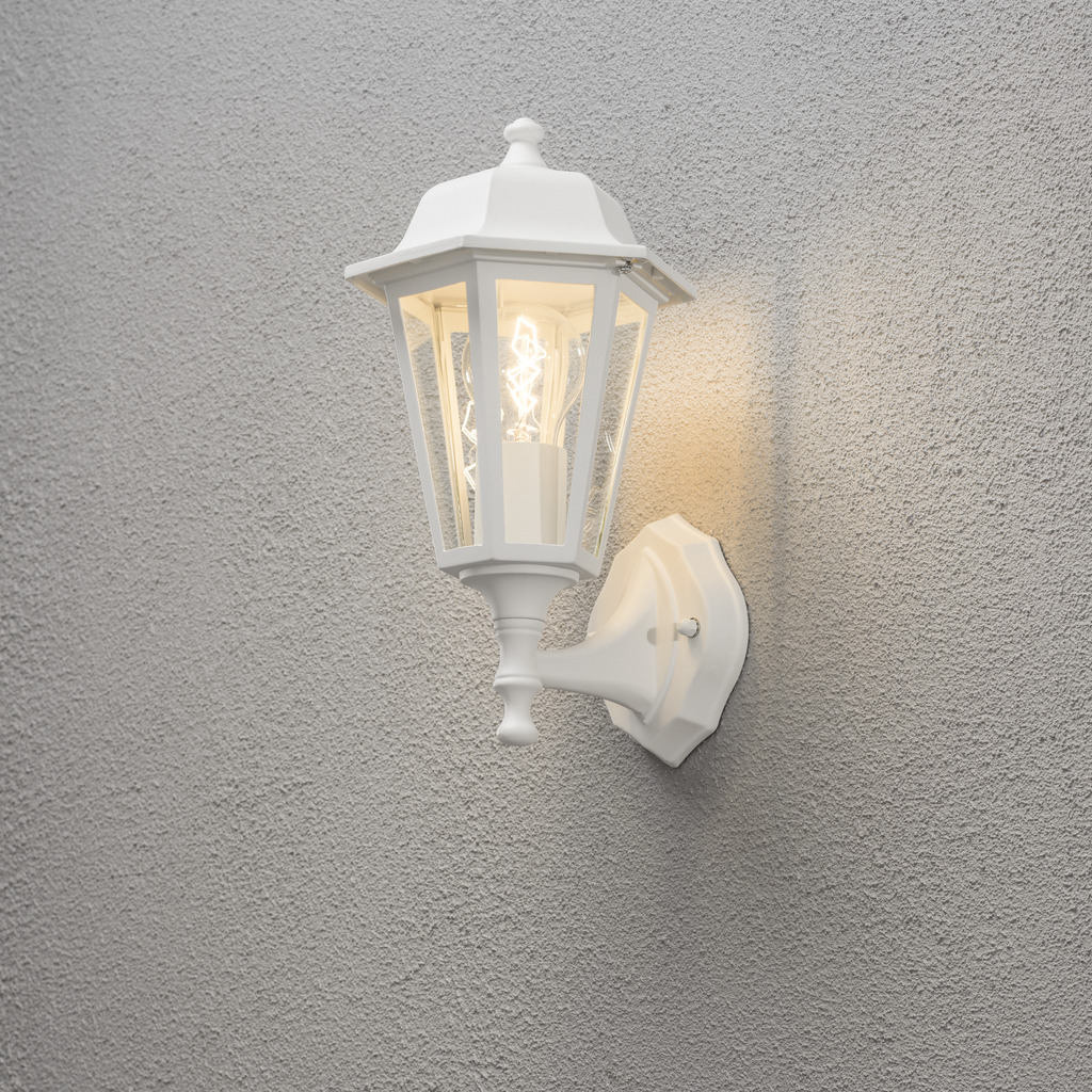 Vägglykta Hvid udendørslampe Fra Konstsmide - Med sit lanterneformede design og klare glaspaneler spreder lampen et varmt og indbydende lys, der er perfekt til indgange, terrasser og gangbroer.