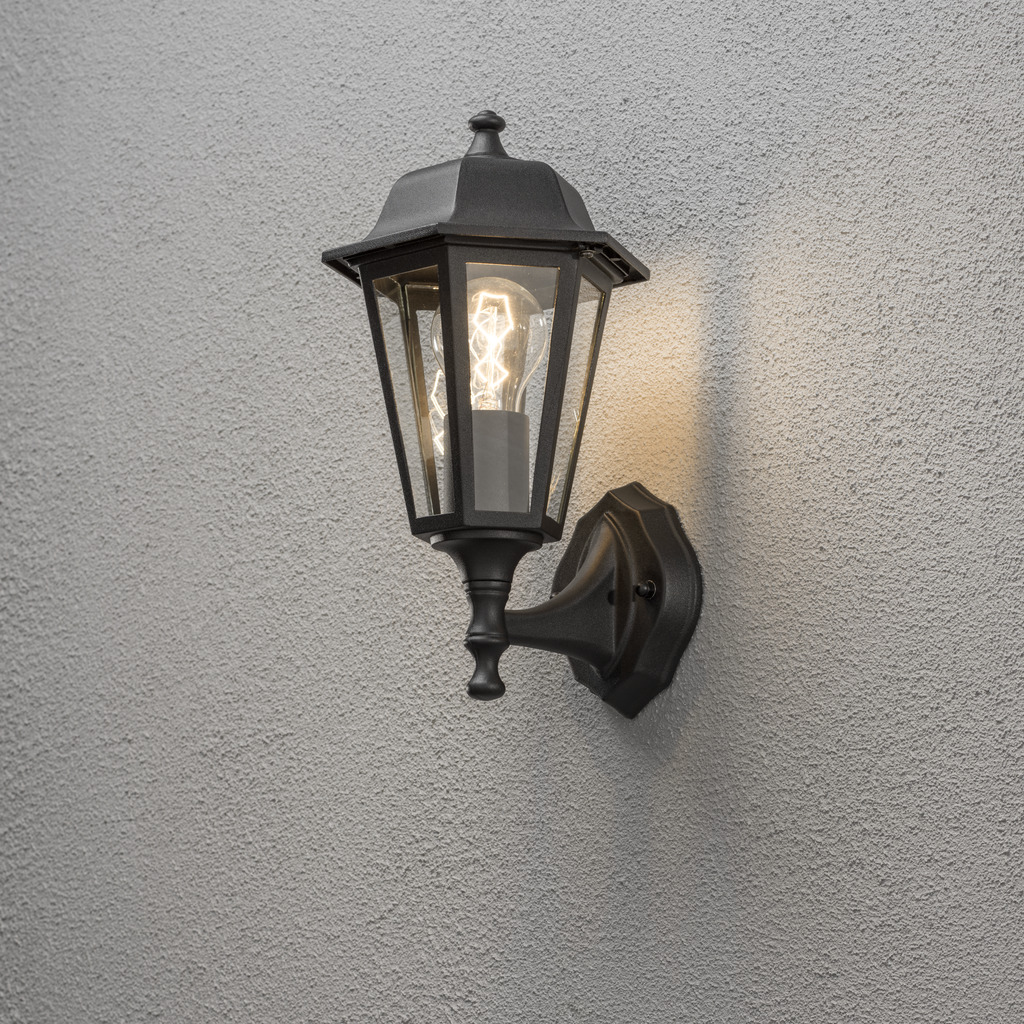 Vägglykta Sort udendørslampe Fra Konstsmide - Med sit lanterneformede design og klare glaspaneler spreder lampen et varmt og indbydende lys, der er perfekt til indgange, terrasser og gangbroer.