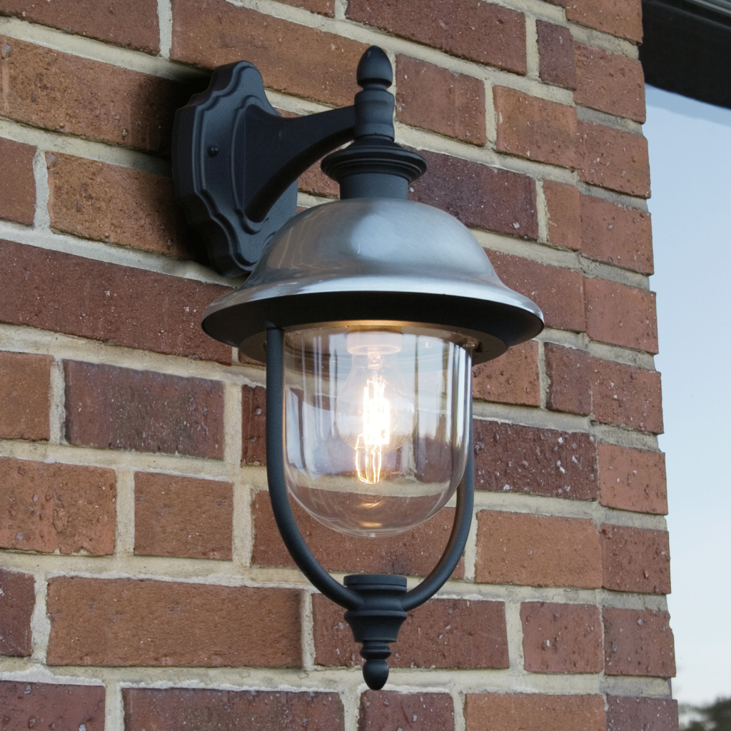Parma Sort udendørslampe Fra Konstsmide - Med sin robuste sorte finish og klare glaskuppel spreder den et varmt og indbydende skær og skaber en indbydende atmosfære ved indgangen eller terrassen.