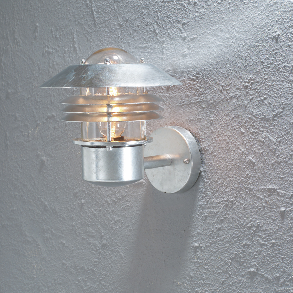 Modena Galvaniseret stål udendørslampe Fra Konstsmide - Med sit beskyttende tag og stilfulde design giver den et behageligt og rettet lys, ideelt til at skabe en tryg og indbydende atmosfære udendørs.
