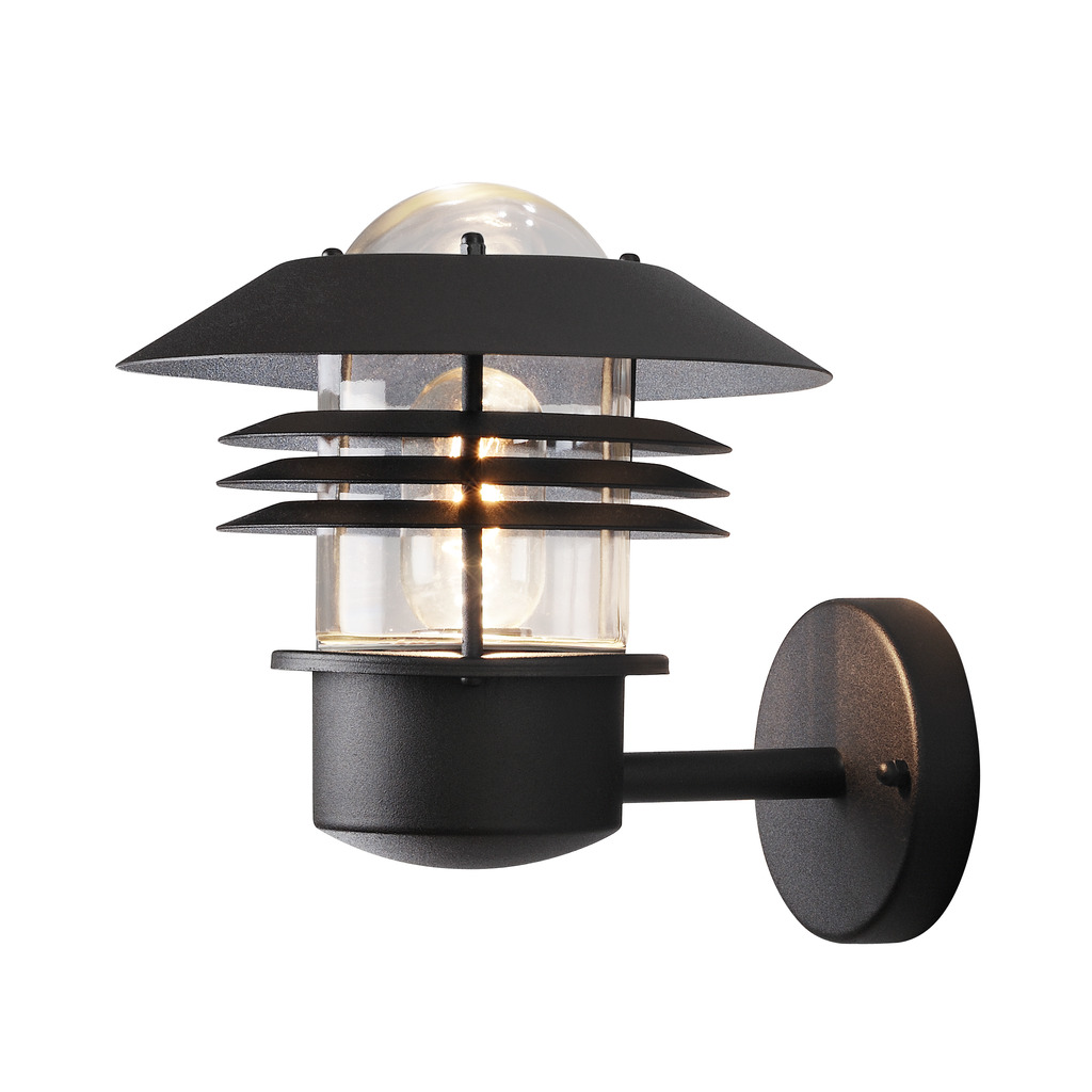Modena Sort udendørslampe Fra Konstsmide - Med sit beskyttende tag og stilfulde design giver den et behageligt og rettet lys, ideelt til at skabe en tryg og indbydende atmosfære udendørs.