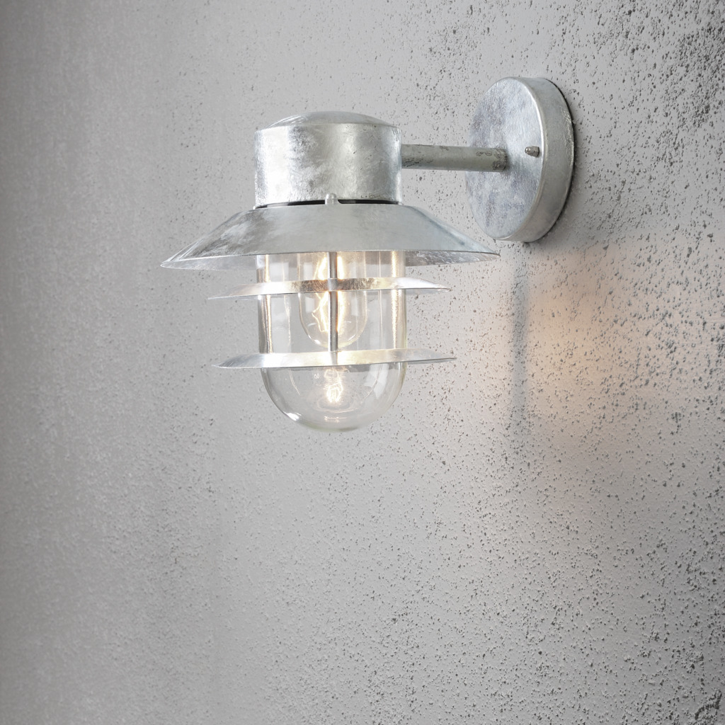 Modena Galvaniseret stål udendørslampe Fra Konstsmide - Med sit beskyttende tag og stilfulde design giver den et behageligt og rettet lys, ideelt til at skabe en tryg og indbydende atmosf&aelig;re udend&oslash;rs.