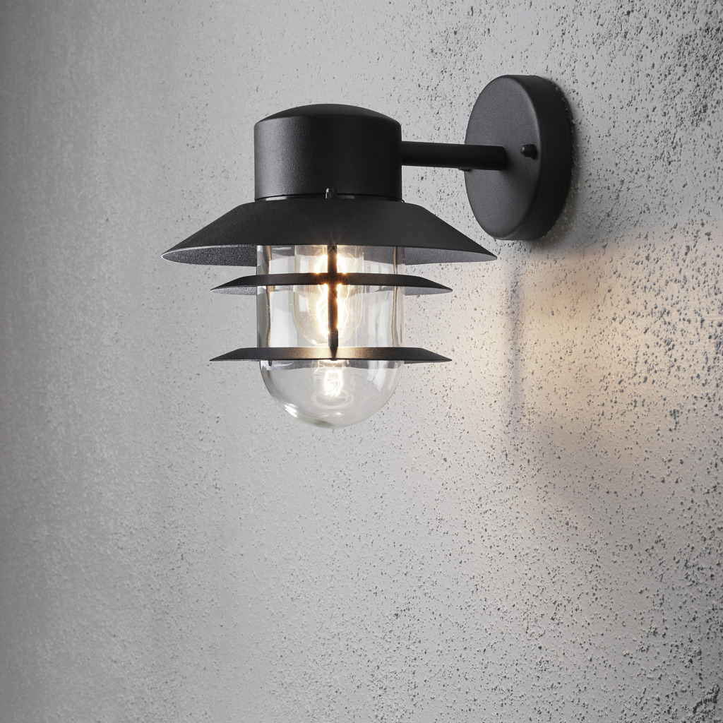 Modena Sort udendørslampe Fra Konstsmide - Med sit beskyttende tag og stilfulde design giver den et behageligt og rettet lys, ideelt til at skabe en tryg og indbydende atmosfære udendørs.