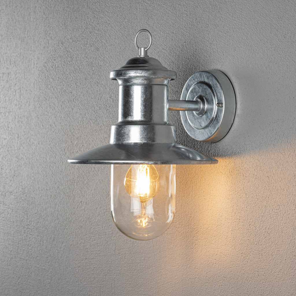Napoli Varmgalvaniseret udendørslampe Fra Konstsmide - Lampens klassiske design med en rund glaskuppel og en bred skærm spreder et varmt og behageligt lys, perfekt til at oplyse indgange og terrasser.