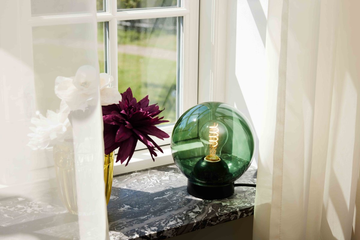 Bubbles 20cm Grøn bordlampe Fra Halo Design - Det grønne glas i kombination med de matsorte metaldetaljer bidrager til en elegance og giver en fin spredning af lys i rummet, når det er oplyst.