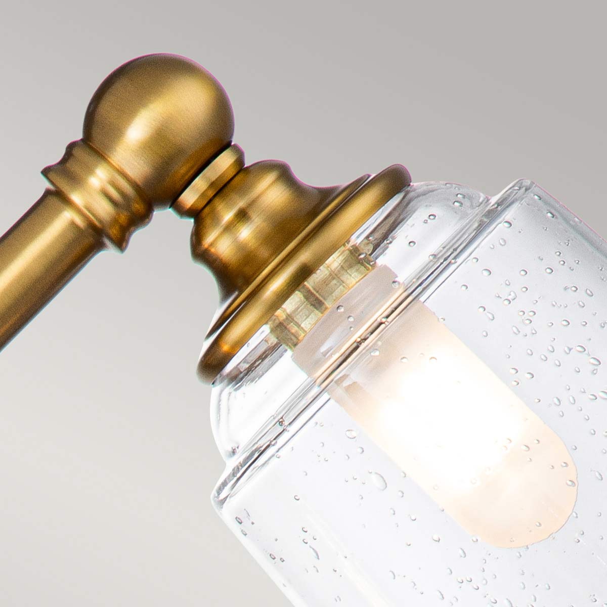 Huguenot Lake 53cm Messing badeværelseslampe Fra Elstead Lighting - De elegante cirkulære detaljer og håndskårne beslag giver en følelse af traditionelt håndværk, mens det klare, strukturerede glas skaber et blødt og indbydende lys.