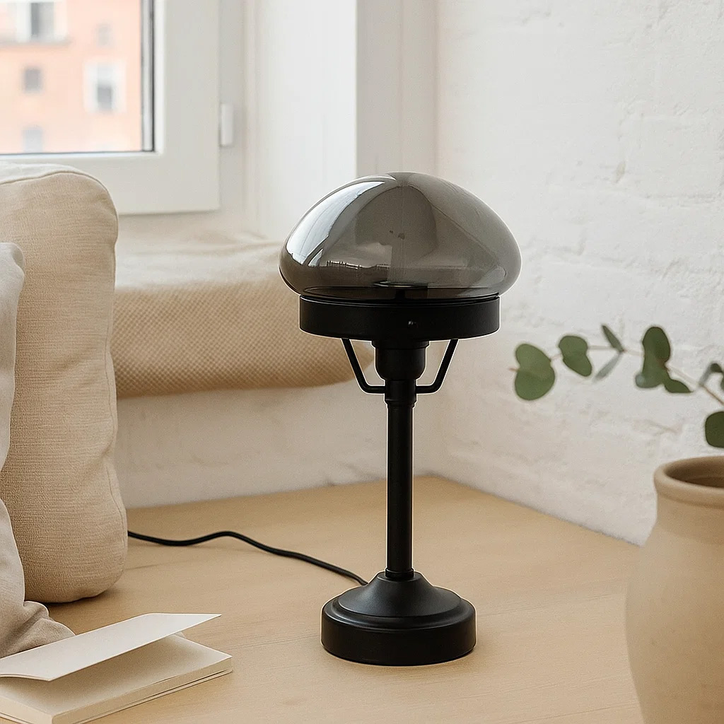 Jas 30cm Sort bordlampe Fra Lampan - Den har en sort metalbase og en kuppelformet lampesk&aelig;rm i r&oslash;get glas, der spreder et bl&oslash;dt og behageligt lys.