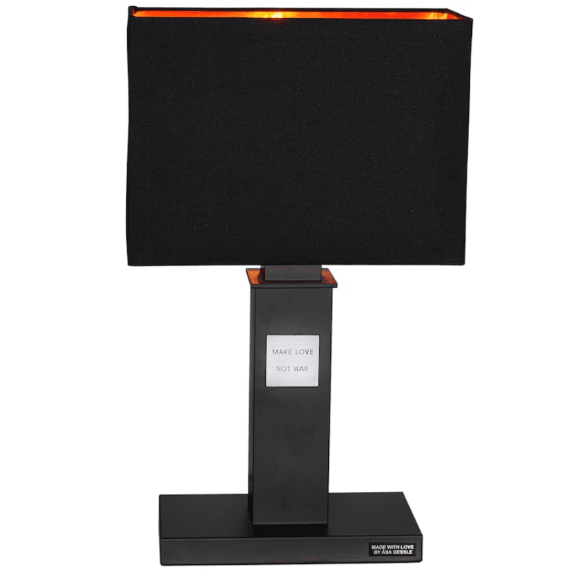 In Love 56cm Sort bordlampe Fra By Rydéns - Den brede, sorte stoflampeskærm harmonerer i kontrast til den smalle lampefod, som er prydet af et metalskilt med teksten "Make love, not war".